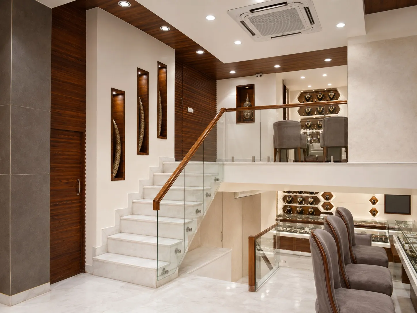 Double-height jewellery showroom in Rajouri Garden with a marble-and-glass staircase, a mezzanine level, and lit display counters