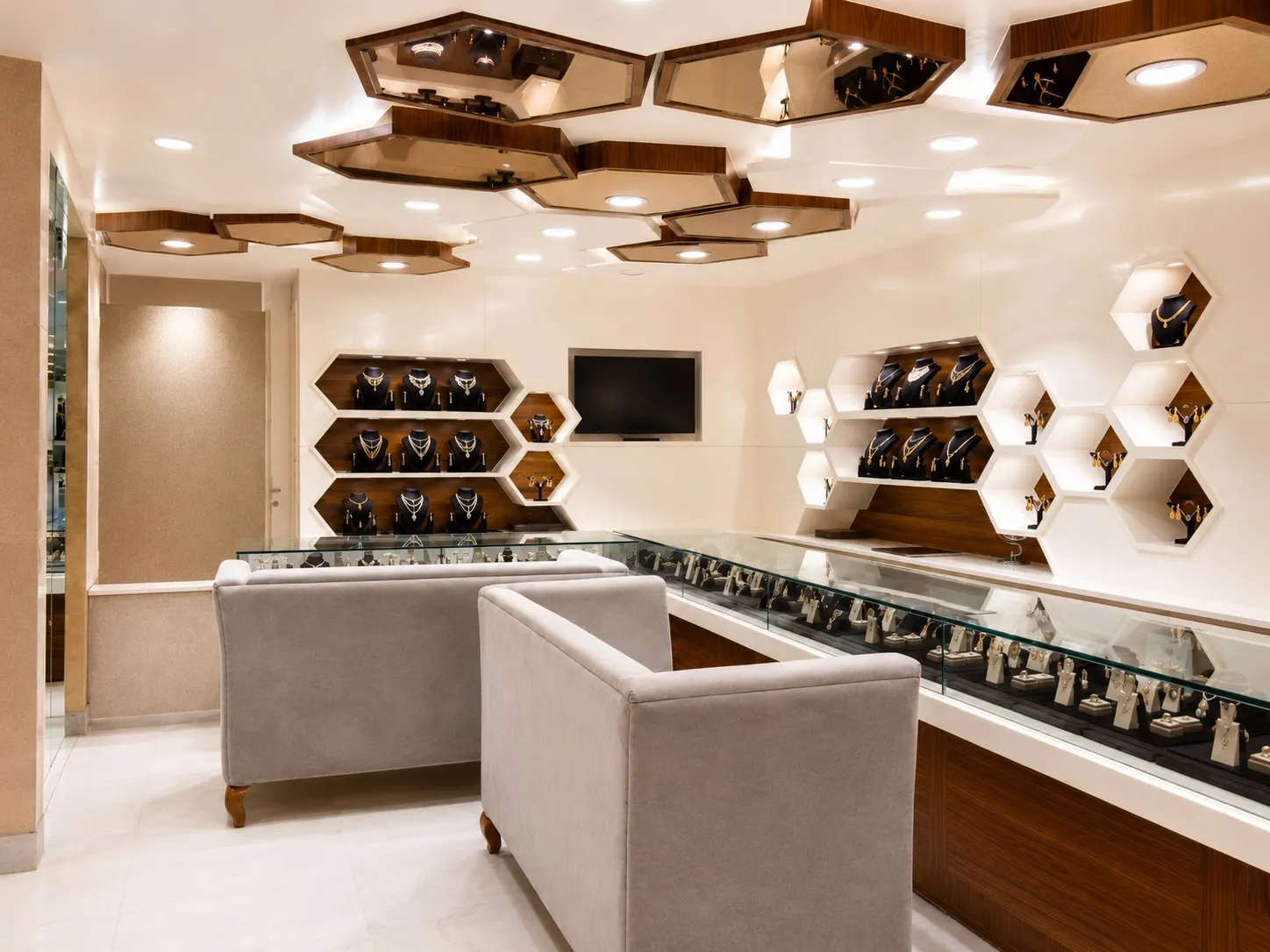 Main showroom floor with a hexagonal mirrored-wood ceiling, honeycomb display niches of gold jewellery, and glass counters