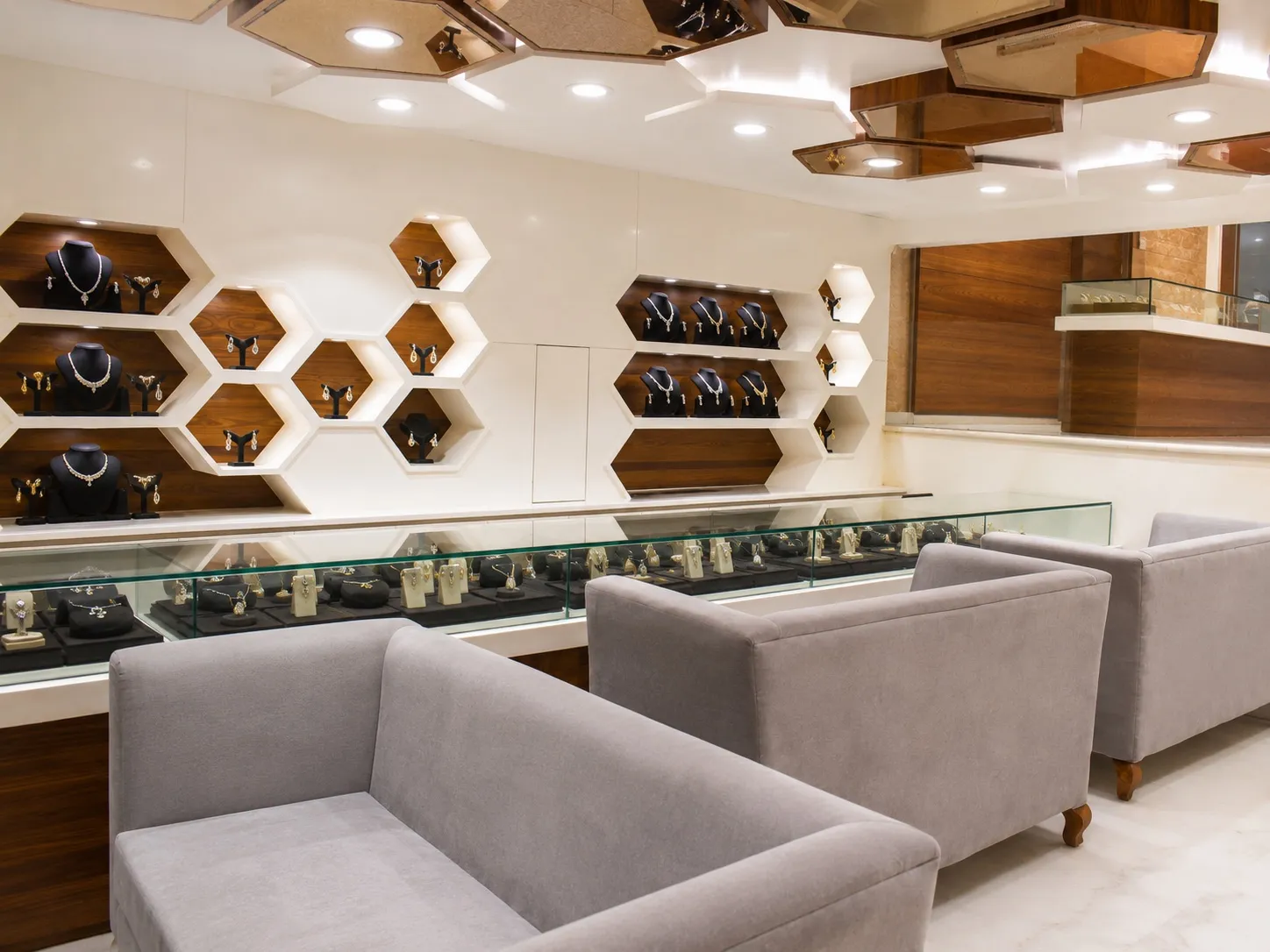 Jewellery display wall with backlit honeycomb niches showing gold necklaces above a run of glass showcase counters