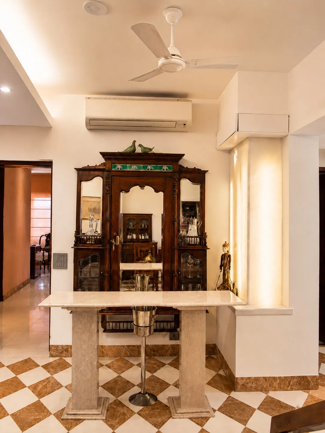 Home bar with a marble counter, an antique mirrored walnut drinks cabinet, silver glassware, and a backlit onyx niche over a checkered marble floor