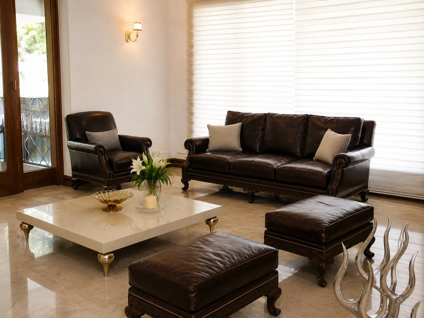 Formal lounge with a dark leather sofa and armchair, a cream lacquer coffee table on brass legs, and sheer layered blinds