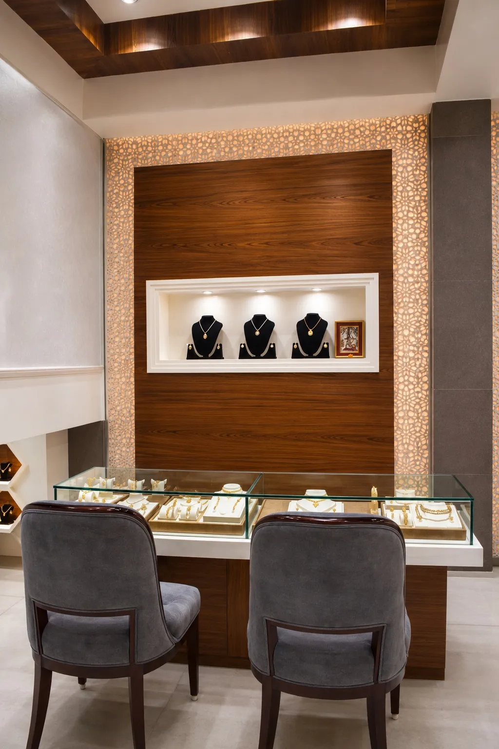 Private consultation counter with a walnut feature wall, a backlit jali border, lit necklace niches, and grey suede chairs