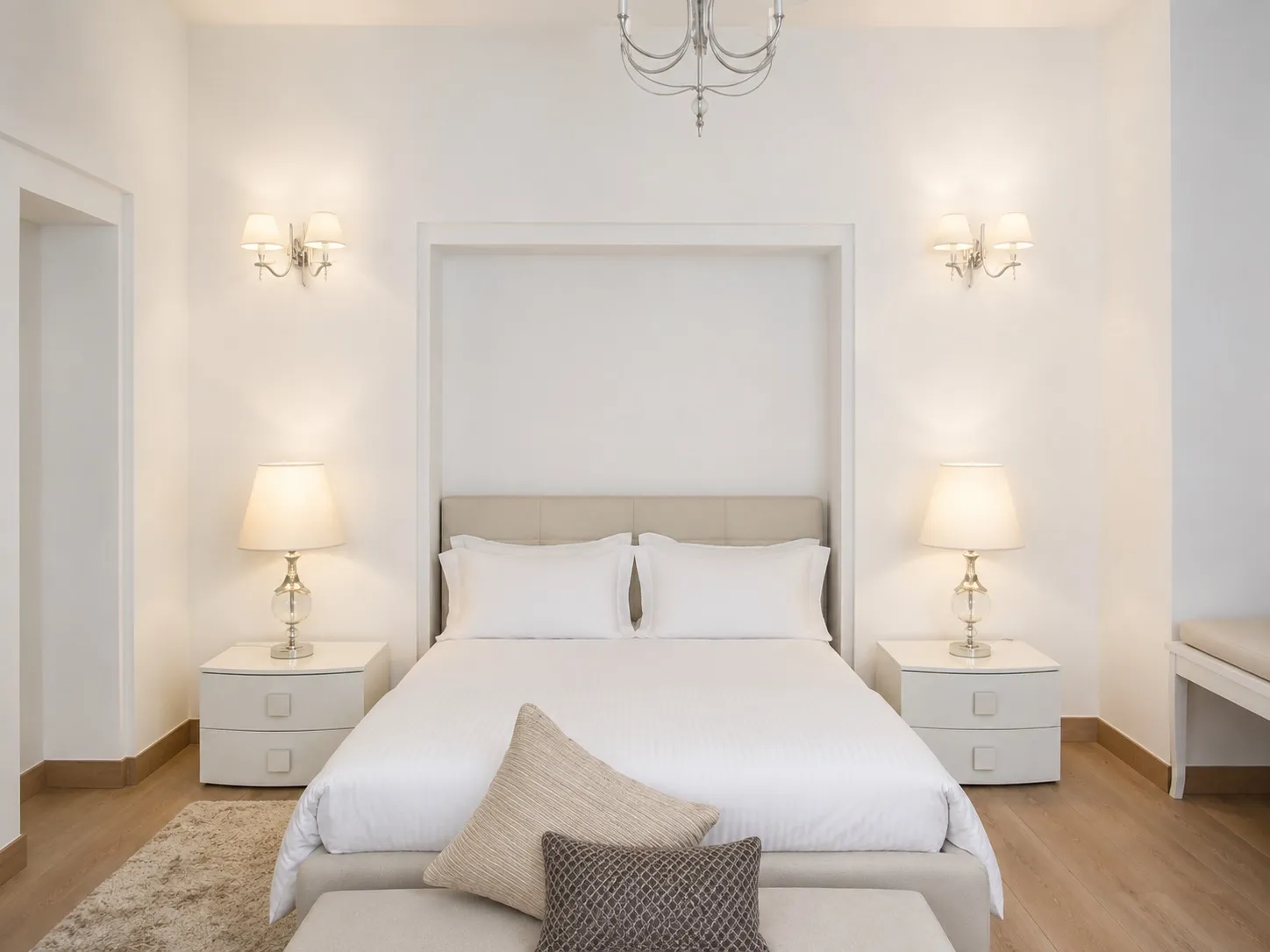 Serene master bedroom in an Anand Niketan residence in soft white and cream, with an upholstered headboard, twin sconces, and matching bedside lamps