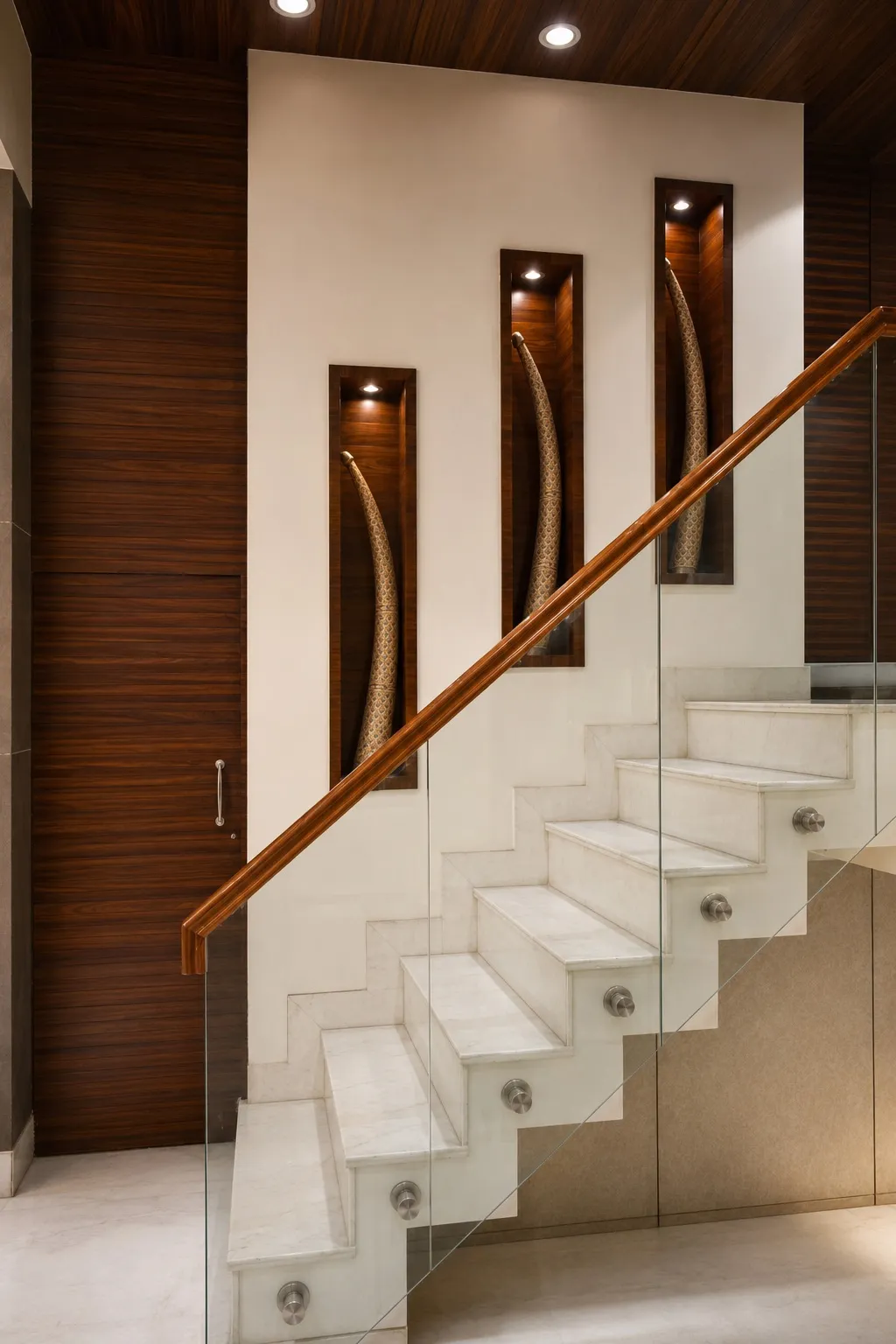 Marble staircase with a glass balustrade and three lit wall niches displaying carved decorative tusks