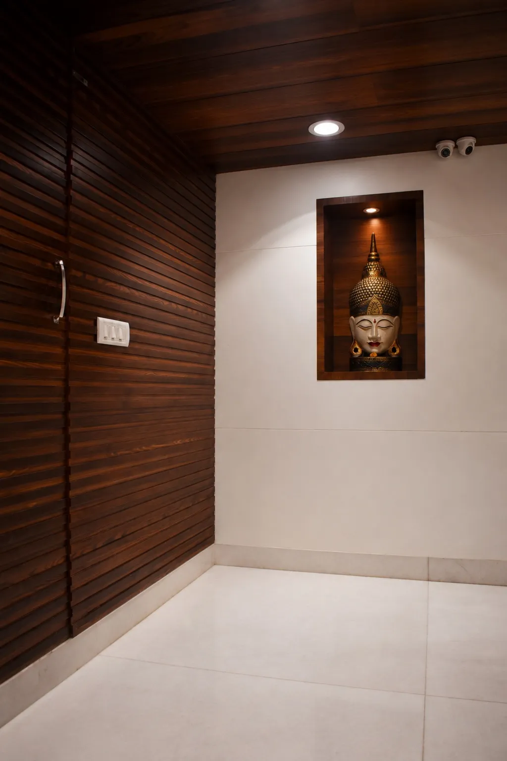 Entrance lobby with a dark wood-slat wall and a backlit niche framing a golden Buddha head sculpture