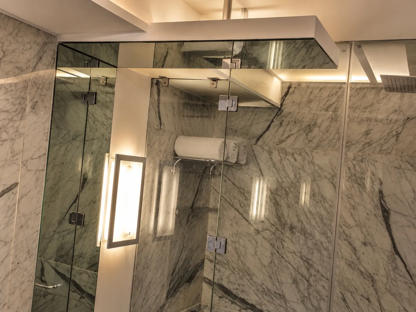Master bathroom shower detail with veined marble walls, a frameless glass enclosure, and a recessed niche