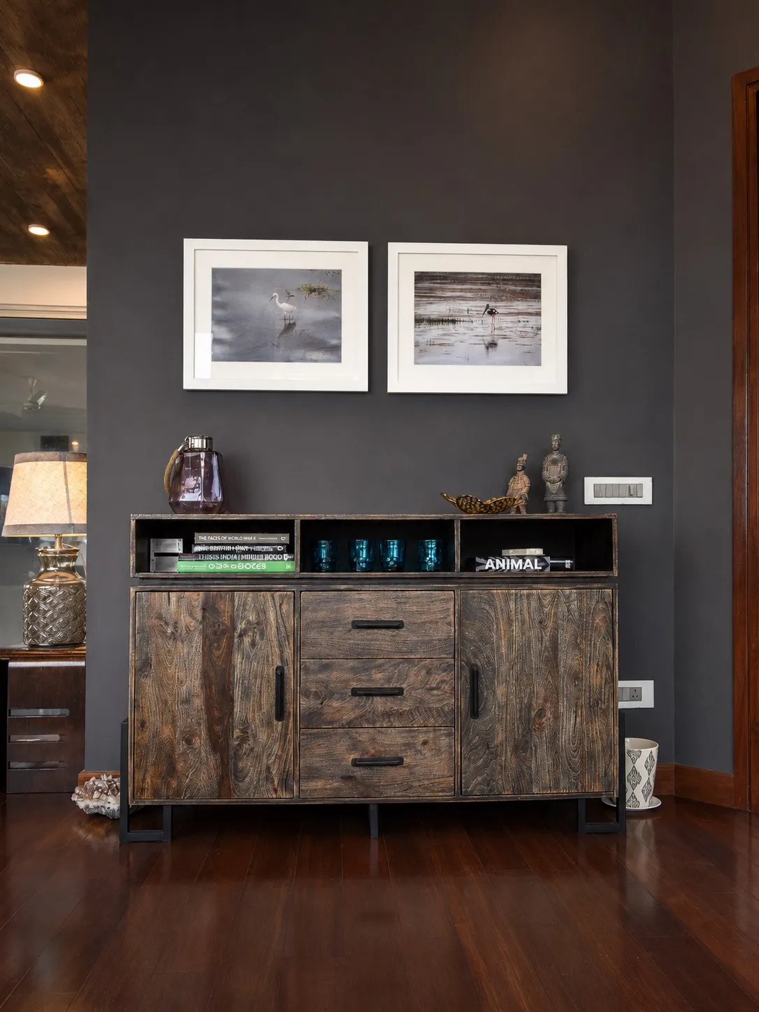 Charcoal-grey wall with a rustic reclaimed-wood sideboard styled with books and objects, below a pair of framed wildlife bird photographs