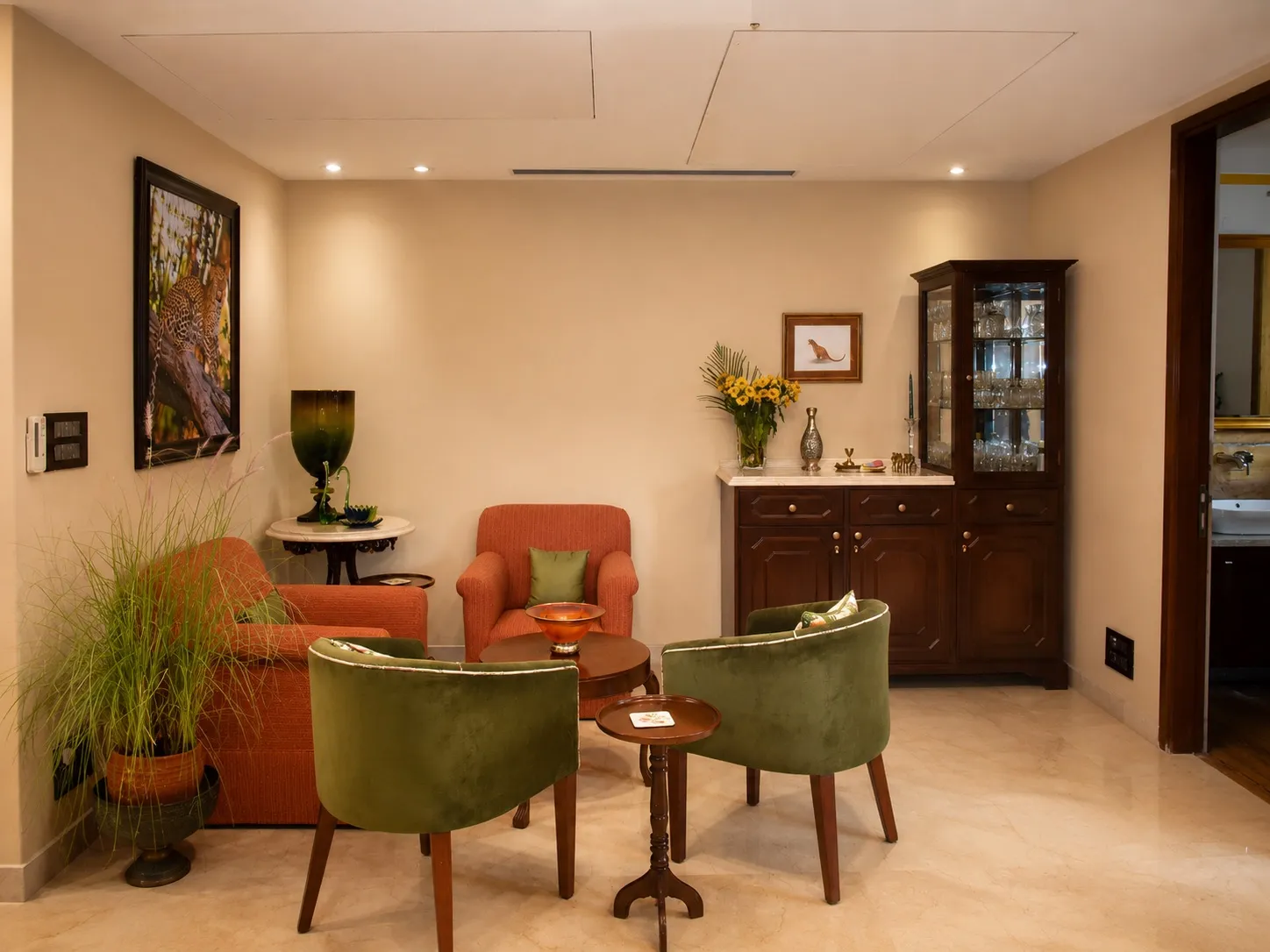 Sitting room with a terracotta sofa, olive-green velvet tub chairs, a dark wood display cabinet, and framed wildlife photography on beige marble