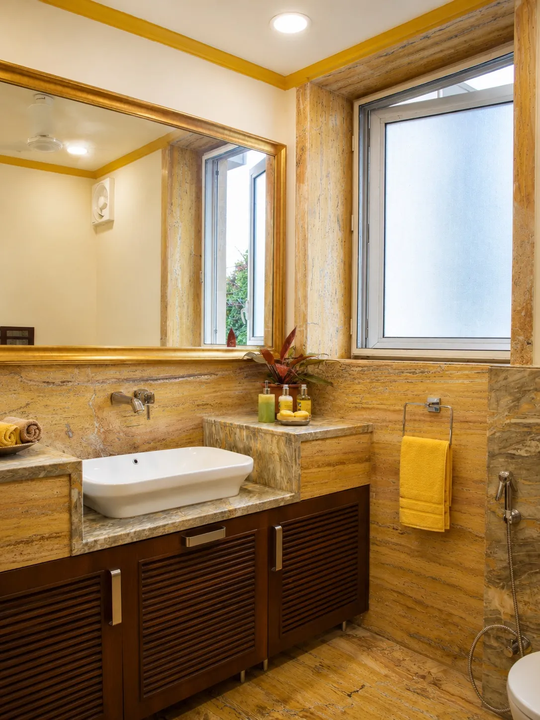 Powder room clad in golden-veined marble with a gold-framed mirror, a white vessel basin, and a yellow hand towel