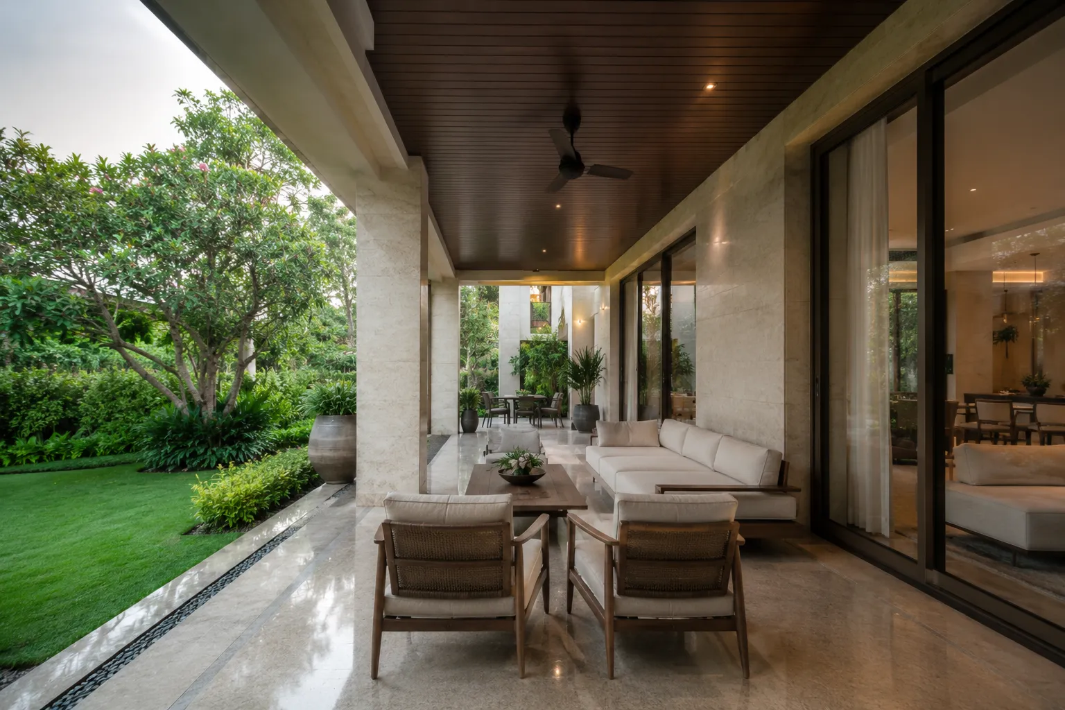 Covered luxury patio with marble floors, wood-slat ceiling, modern beige seating, and a view of a lush green lawn.