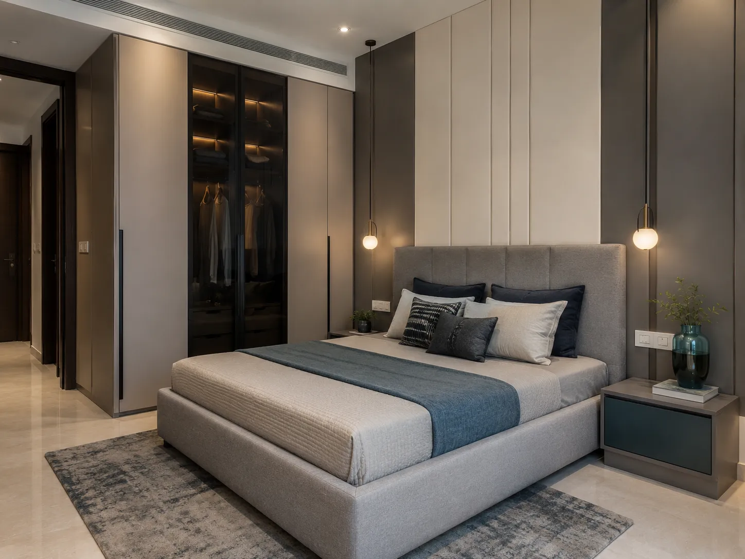 A luxury bedroom with a taupe upholstered bed, blue runner, brass pendant lights, and a dark glass-front wardrobe with warm interior lighting.