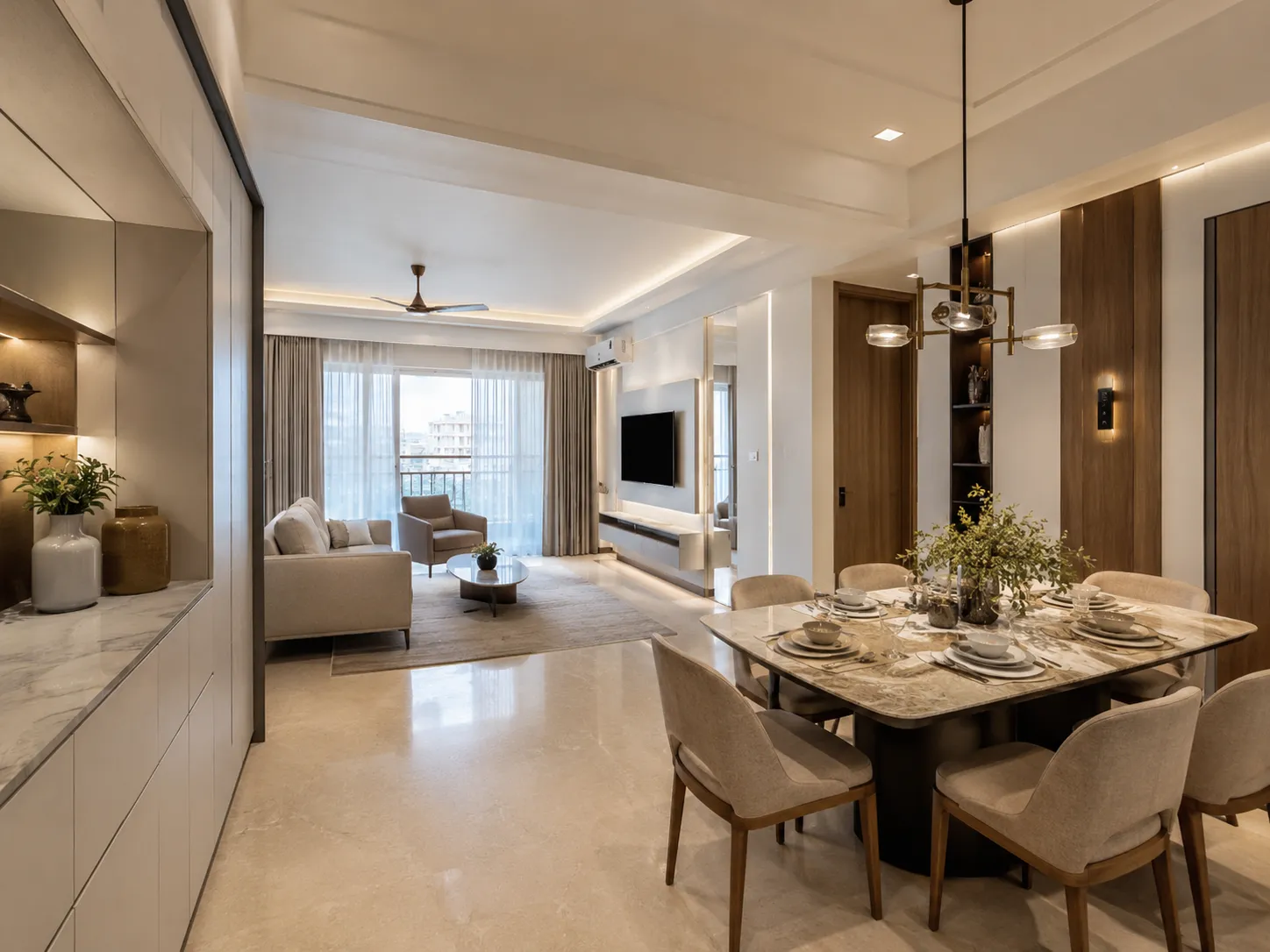Open-plan living and dining area in a Delhi apartment featuring a marble dining table, beige upholstered chairs, modern brass chandelier, and cove ceiling lighting.