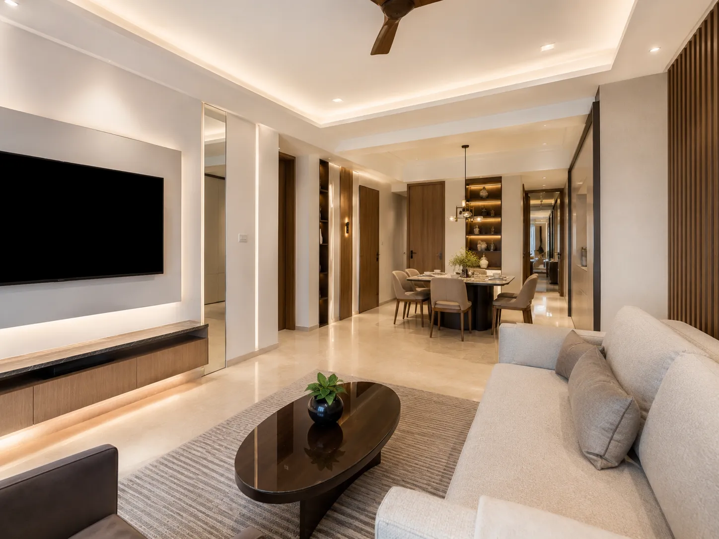 Living room with a wall-mounted TV unit, cove lighting, oval dark wood coffee table, beige sofa, and a vertical mirror panel reflecting the space.