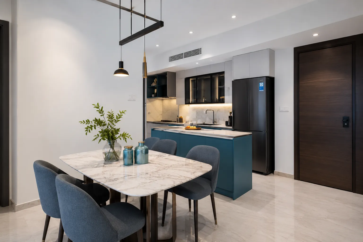 An open-plan space with a marble-top dining table, blue upholstered chairs, and a kitchen featuring a teal island and dark glass upper cabinets.