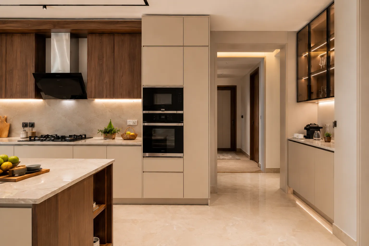 Straight-on view of a kitchen showing a built-in oven tower in matte beige cabinetry, dark walnut upper cabinets, and a glass-front display unit with interior LED lighting.
