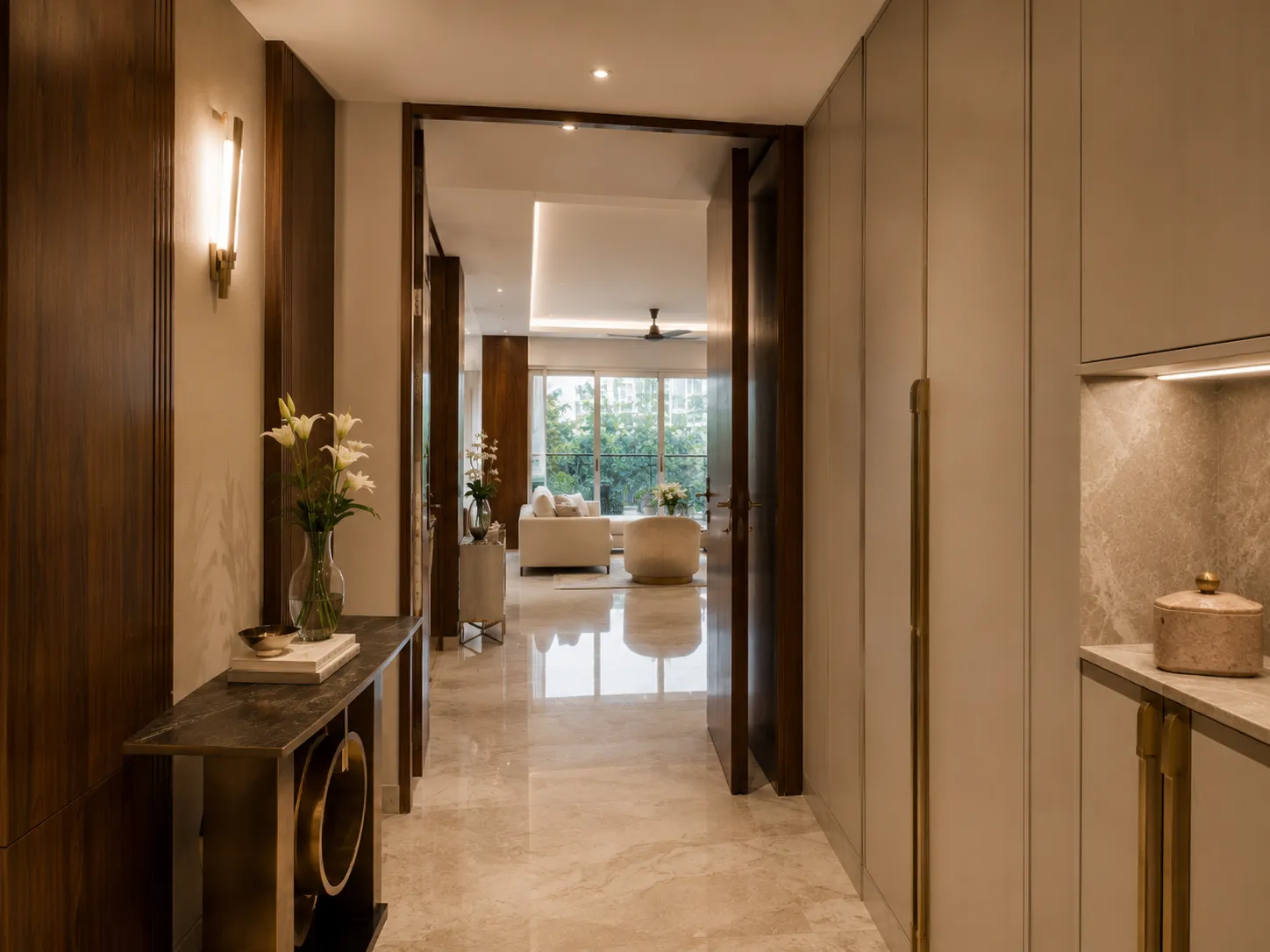 Luxury hallway with reflective marble floors, dark wood paneled walls, a slim marble console table with brass rings, and built-in beige wardrobes.